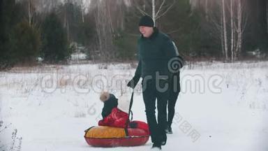 一家人在森林附近的户外跑步和玩耍-男人把他的孩子卷在充气雪橇上